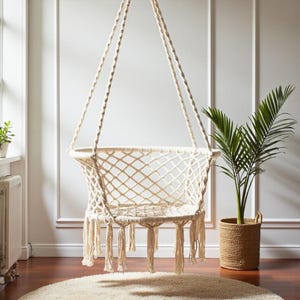 May include: A cream macrame hanging chair with a woven seat and fringe detail, suspended from the ceiling by thick, braided ropes. A potted plant in a woven basket adds greenery. The chair is a stylish addition to any room.