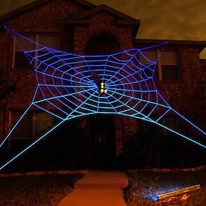 May include: A large blue spider web decoration is strung up in front of a house. The web is lit up with blue lights, creating a spooky and festive Halloween atmosphere.