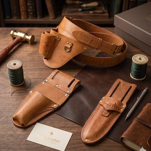 Puede incluir: Un cinturón de herramientas de cuero color canela con hebilla y anilla de latón, con el texto Liftha leather grabado. Incluye dos fundas de cuero separadas, dos carretes de hilo verde, un martillo de latón, un portaminas y una tarjeta de visita.