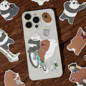May include: A collection of cartoon bear stickers, including panda and polar bear designs, are scattered around a smartphone. The stickers feature various poses and activities, such as riding a bicycle and eating. The phone has multiple camera lenses.