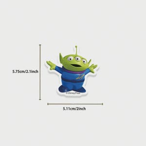 May include: A green alien character with three eyes, wearing a blue uniform with a purple collar. The character is 2.1 inches tall and 2 inches wide. The Disney/Pixar logo is visible. The image is on a white background.