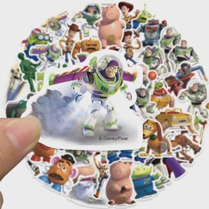May include: A collection of colorful Toy Story character stickers, including Buzz Lightyear, Woody, and others. The stickers are in various shapes and sizes, with a white background. The Disney/Pixar logo is visible on one sticker.