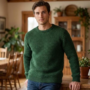 Könnte beinhalten: Ein grüner Pullover mit Rundhalsausschnitt und strukturiertem Strickmuster. Der Pullover hat einen gerippten Saum und Bündchen. Die Person trägt eine blaue Jeans. Der Pullover ist einfarbig und scheint aus einem weichen Material zu sein.