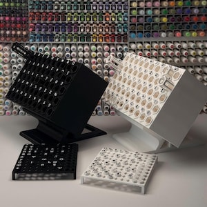 Peut inclure: Un organisateur de bureau noir et un blanc, inclinés, présentant chacun un motif en grille hexagonale avec divers symboles et lettres imprimés sur la surface. Deux plateaux carrés plats assortis sont placés devant les supports.