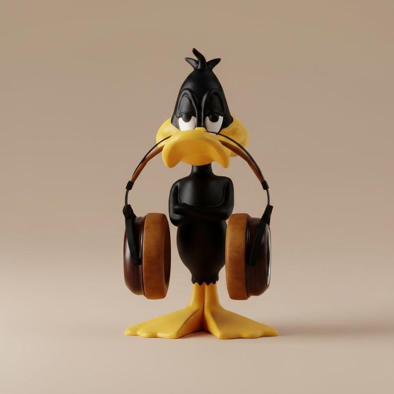 May include: A black Daffy Duck figurine with a yellow beak and feet, wearing brown headphones. The cartoon character has its arms crossed and a slightly annoyed expression. The background is a solid beige color.