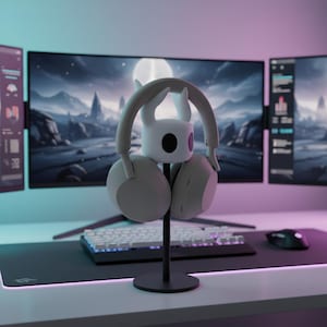 May include: A white and gray headset rests on a black stand, with a white character figure. The stand is on a desk with a keyboard, mouse, and multiple computer monitors displaying a landscape scene. The scene is illuminated with blue and pink lighting.