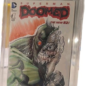 Puede incluir: Un cómic calificado titulado "Superman Doomed #1". La portada presenta una ilustración detallada de un personaje monstruoso con una combinación de colores verde y gris. El cómic está encerrado en un soporte protector con una calificación de 9.8.