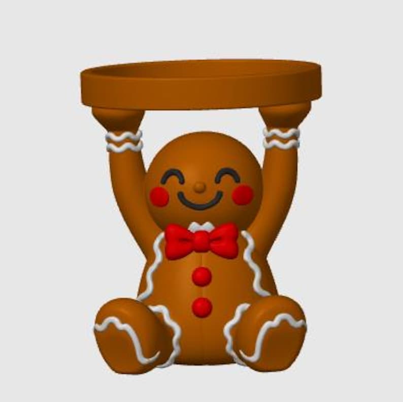 May include: A brown gingerbread person figurine holding a circular tray above its head. The figure features white icing-style trim, a red bow tie, two red buttons, and red cheeks. The gingerbread person has a smiling face with closed eyes.