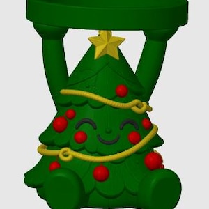 May include: A green Christmas tree-shaped candle holder featuring a smiling face, red ornaments, and a yellow garland. The tree is topped with a yellow star and has two arms extending upward to support a circular green platform at the top.