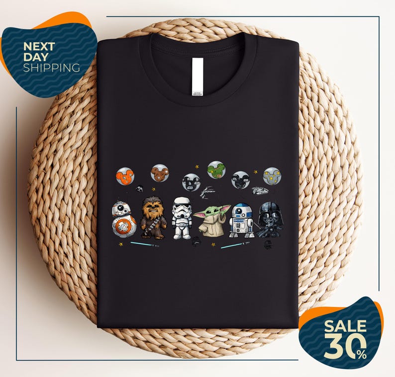 a black t-shirt with a graphic design of various Star Wars characters, including Star Wars, Darth Vader, and Baby Yoda, arranged in a row.