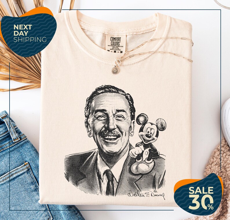 a t-shirt with a black and white illustration of Walt Disney, along with a necklace and a Mickey Mouse plush toy. The t-shirt is displayed on a white background, and there are some jeans and a sweater visible in the background.