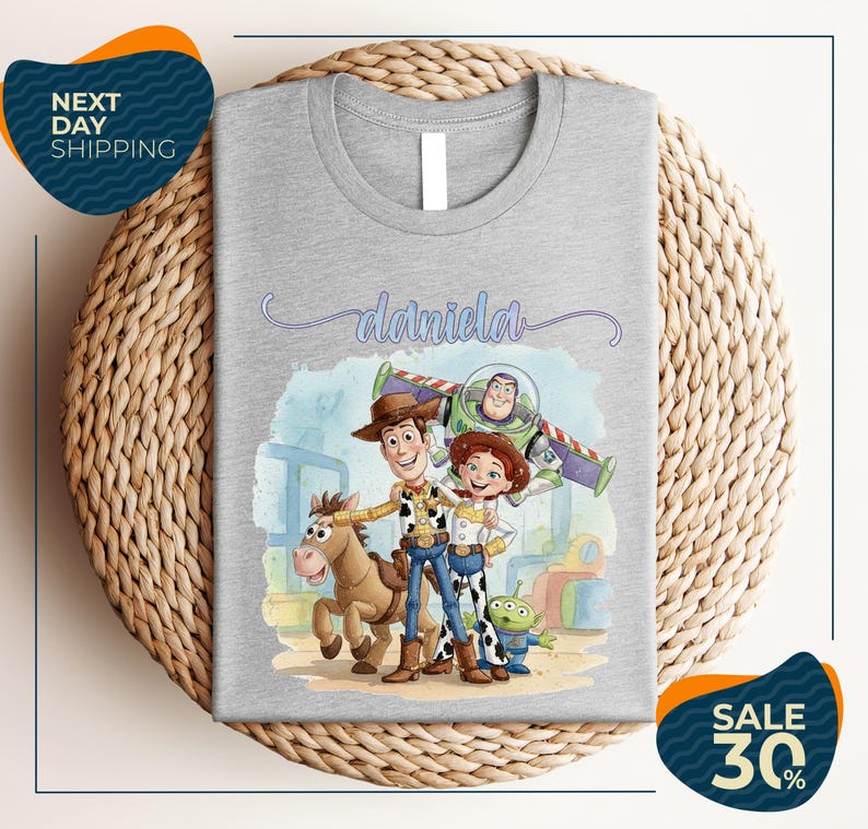 a gray t-shirt with a cartoon illustration of characters from the Toy Story franchise, including Woody, Buzz Lightyear, and an alien character. The t-shirt is displayed on a woven placemat, and there are two sale signs indicating a 30% discount on the item.