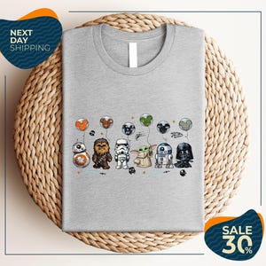 A gray t-shirt with a graphic design featuring various Star Wars characters, including Chewbacca, Bond, Baby Yoda, Darth Vader, and others, along with balloons.