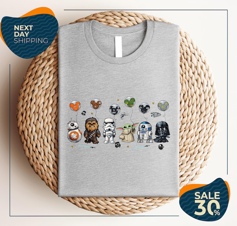A gray t-shirt with a graphic design featuring various Star Wars characters, including Chewbacca, Bond, Baby Yoda, Darth Vader, and others, along with balloons.