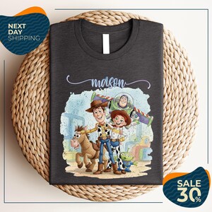a t-shirt with a cartoon illustration of characters from the Toy Story franchise, including Woody, Buzz Lightyear, and a horse.