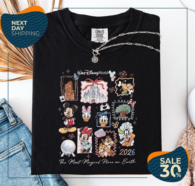 a black t-shirt with a Disney-themed graphic design, including various Disney characters and landmarks. The t-shirt is displayed on a white background, and there are jeans and a necklace visible in the foreground.