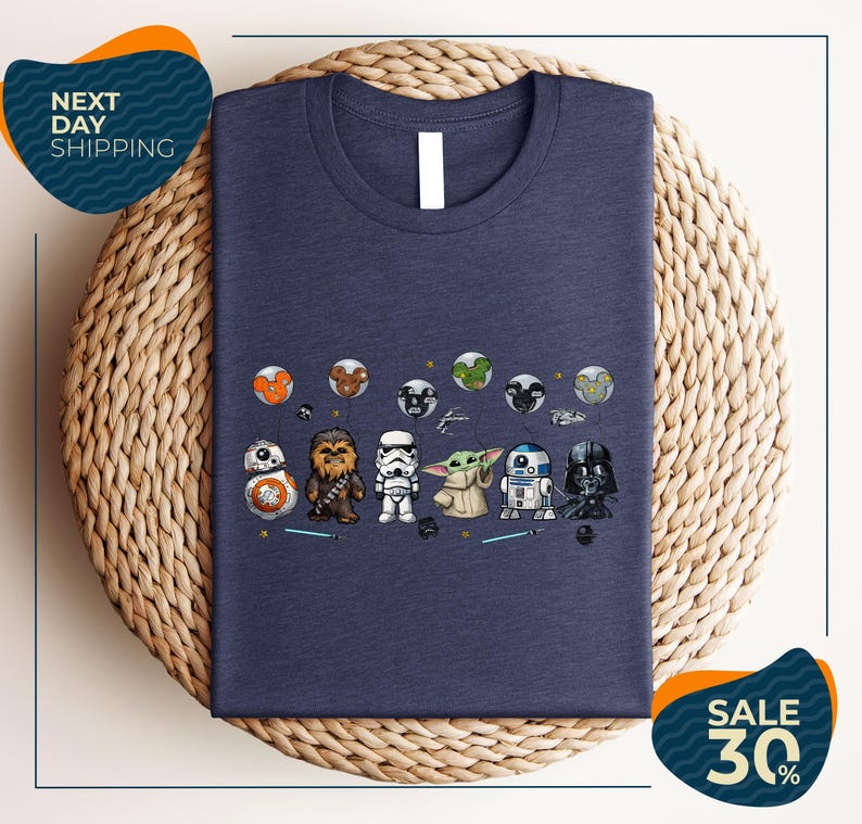 a blue t-shirt with a graphic design of various Star Wars characters, including Chewbacca, Stormtrooper, Baby Yoda, Darth Vader, and others, arranged in a row.