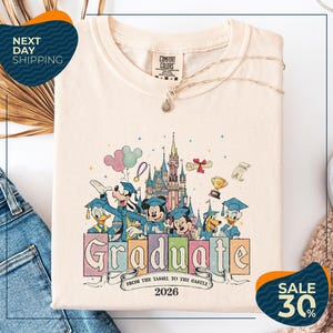 a white t-shirt with a colorful graphic design depicting Disney characters in graduation attire, along with the text "Graduate from the Tasse to the Castle" and the year "2026". The t-shirt is displayed on a white background, and there are jeans visible in the background.