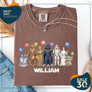 A brown t-shirt with a graphic design featuring various characters from the Star Wars franchise, including Chewbacca, Darth Vader, Stormtrooper, and Yoda, along with colorful balloons. The text "WILLIAM" is displayed below the characters, and there are two sale signs indicating a 30% discount on the t-shirt.