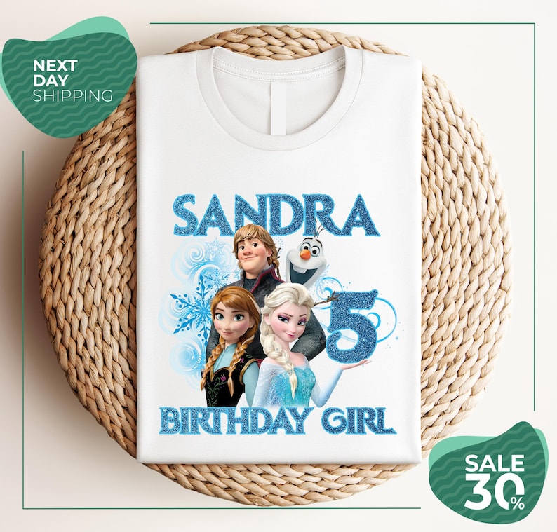 A white t-shirt with a design featuring characters from the Disney movie Frozen, specifically Elsa, Olaf, and Anna, along with the text "SANDRA BIRTHDAY GIRL".