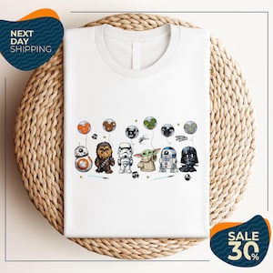 A white t-shirt with a graphic design featuring various Star Wars characters, including Chewbacca, Stormtrooper, Darth Vader, and Baby Yoda, along with balloons and stars.