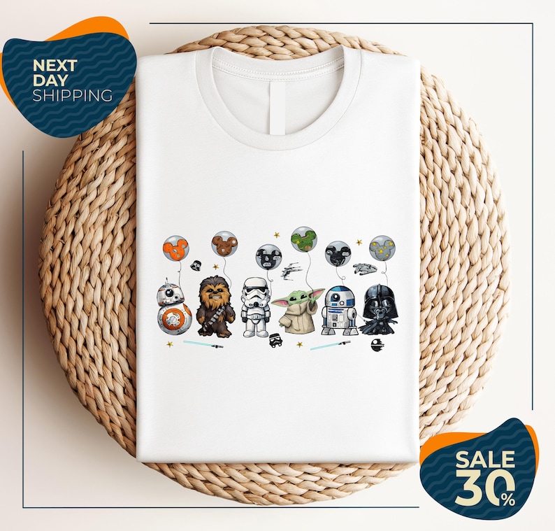 A white t-shirt with a graphic design featuring various Star Wars characters, including Chewbacca, Stormtrooper, Darth Vader, and Baby Yoda, along with balloons and stars.