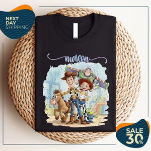 a black t-shirt with a colorful illustration of characters from the Toy Story movie, including Woody, Buzz Lightyear, and an alien. The t-shirt is displayed on a woven placemat, and there are two sale signs indicating a 30% discount on the item.