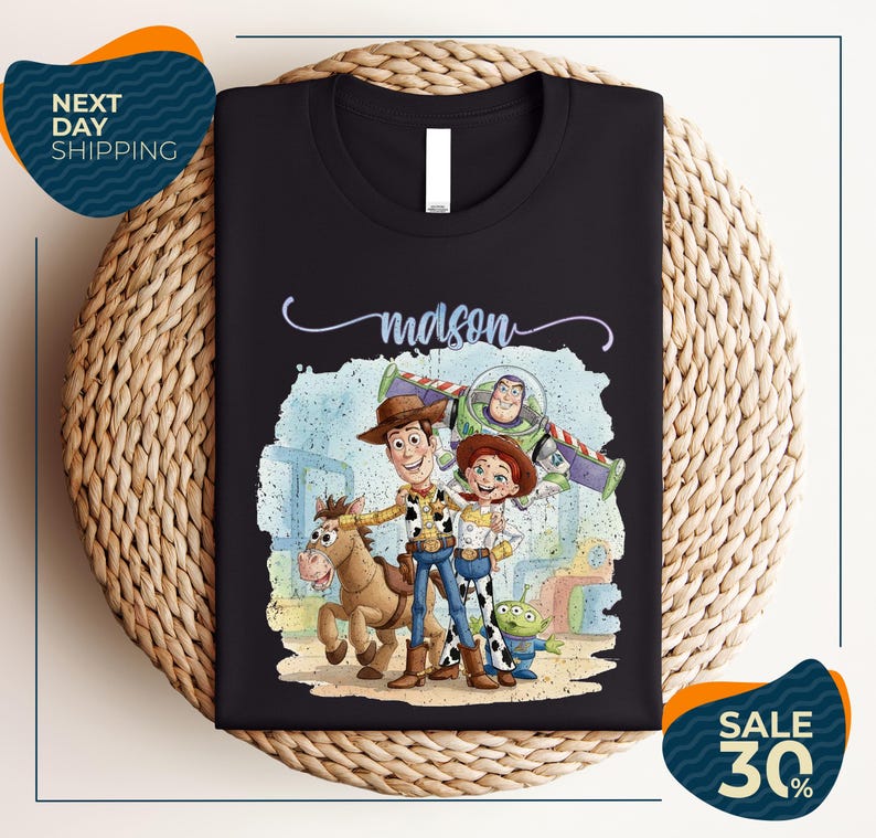 a black t-shirt with a colorful illustration of characters from the Toy Story movie, including Woody, Buzz Lightyear, and an alien. The t-shirt is displayed on a woven placemat, and there are two sale signs indicating a 30% discount on the item.