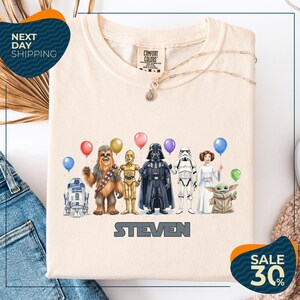 a t-shirt with a graphic design of various Star Wars characters, including Chewbacca, Darth Vader, Stormtrooper, and Yoda, along with balloons. The t-shirt is displayed on a white background, and there are two sale signs indicating a 30% discount on the item.