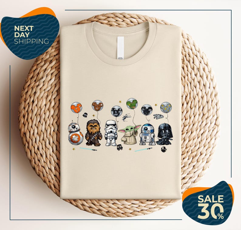 a beige t-shirt with a graphic design of various Star Wars characters, including Chewbacca, Stormtrooper, Darth Vader, and Baby Yoda, along with other Star Wars-themed elements.