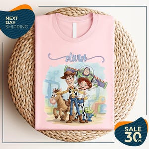A pink t-shirt featuring characters from the Toy Story movie, including Woody, Buzz Lightyear, and a girl, along with a horse and a dog.