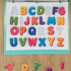 May include: A light blue three-ring binder containing a white sheet with colorful, three-dimensional alphabet letters attached by hook-and-loop fasteners. Additional loose letters spelling the word ARTE are positioned below the binder.