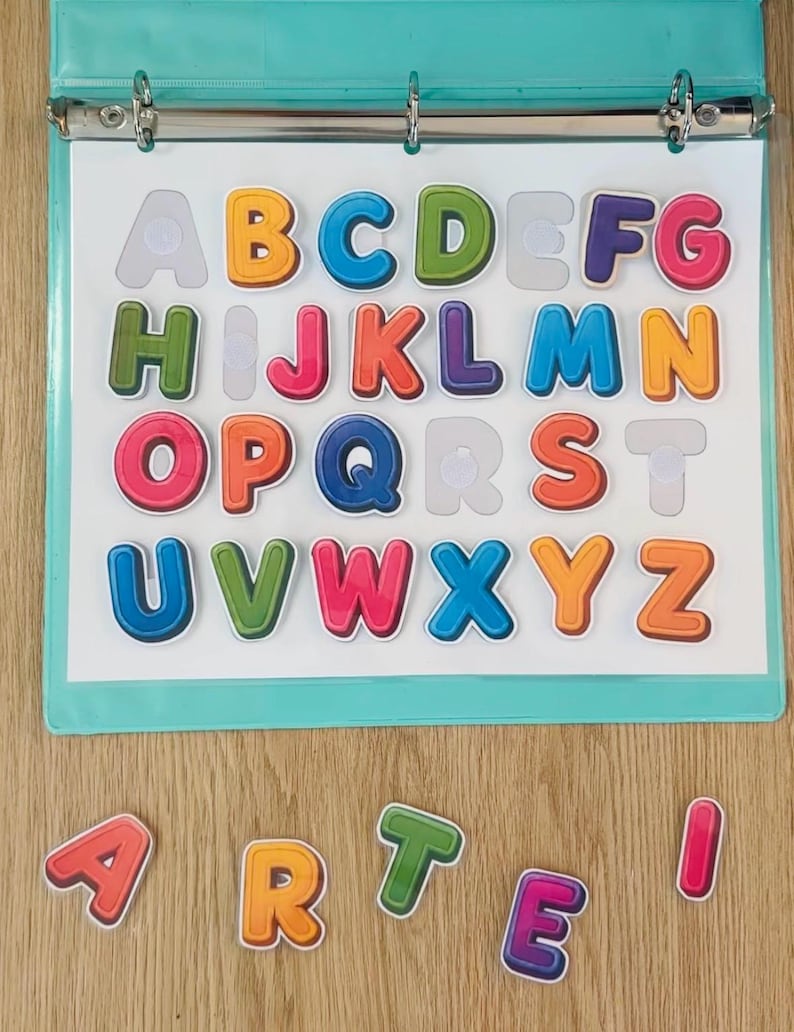 May include: A light blue three-ring binder containing a white sheet with colorful, three-dimensional alphabet letters attached by hook-and-loop fasteners. Additional loose letters spelling the word ARTE are positioned below the binder.