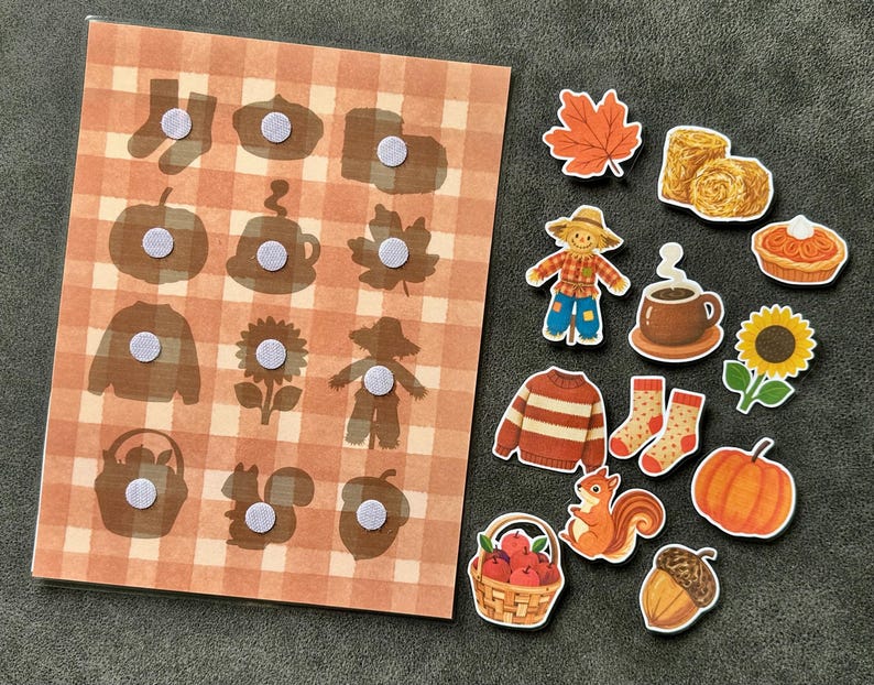May include: A rectangular board with a light orange and white plaid pattern featuring twelve circular hook-and-loop fasteners, accompanied by twelve separate autumn-themed cutouts including a scarecrow, pumpkin, sunflower, squirrel, acorn, and sweater.
