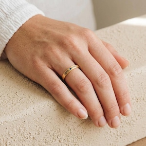 May include: A gold ring with a delicate leaf pattern and a small blue gemstone. The ring is on a hand with a neutral background. The ring is a simple band style, perfect for everyday wear.
