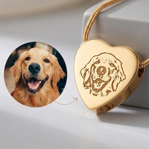 Könnte beinhalten: Goldfarbene herzförmige Anhänger-Halskette mit detaillierter Gravur eines Golden Retriever Hundes. Der Anhänger ist mit einer goldenen Kette verbunden. Ein rundes Foto des Hundes befindet sich neben dem Anhänger.