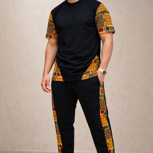 以下が含まれることがあります： カラフルな模様のアクセントが付いた黒いTシャツと黒いスウェットパンツ。半袖シャツは模様入りの袖と前面に模様入りのパネルが付いています。スウェットパンツは側面に模様入りのストライプが入っています。黒いスニーカーでコーディネートが完成しています。