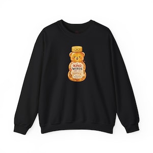 May include: A black crewneck sweatshirt featuring a central graphic of a honey bear bottle. The bottle has a yellow cap and contains golden honey. The text reads: KIND WORDS ARE LIKE HONEY, Proverbs 16:24, with small floral and honey dipper accents.