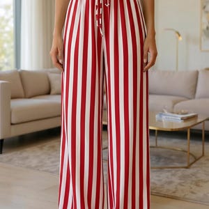 Könnte beinhalten: Hoch taillierte Hose mit weitem Bein und einem markanten vertikalen Streifenmuster in Rot und Weiß. Die Hose verfügt über einen elastischen Bund mit einem passenden Kordelzug aus Stoff in der Mitte, was eine lockere Silhouette ergibt.