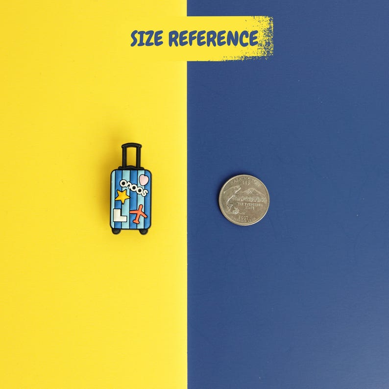 May include: A blue and light blue striped suitcase charm featuring a black handle and colorful stickers including a yellow star, a red airplane, and the text "onoos" next to a US quarter coin for size reference on a split yellow and blue background.