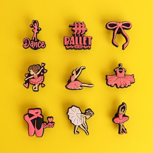 May include: A set of nine pink and black shoe charms featuring ballet themes, including a dancer silhouette with the word Dance, the word Ballet, a bow, a ballerina, a tutu on a hanger, ballet slippers, and various dancing figures.