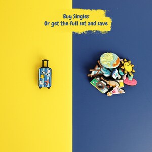 May include: A blue striped suitcase charm with a yellow star and red airplane icon, alongside a collection of colorful summer-themed charms including a camera, sun, and beach chair. Text reads: Buy Singles Or get the full set and save.