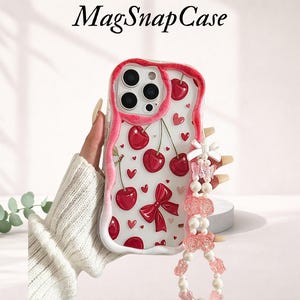 Könnte beinhalten: Transparente Handyhülle mit einem Design aus roten und rosa Kirschen. Die Hülle hat einen pinkfarbenen Rand, Kirschen, Herzen und eine Schleife. Sie hat eine pinkfarbene Perlenkette mit einer Schleife und einem Schmetterlingsanhänger. Der Text "MagSnapCase" steht oben.