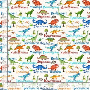 May include: A white fabric featuring a repeating pattern of colorful dinosaurs including Spinosaurus, Triceratops, and Brachiosaurus, with their names printed in various colors. A ruler showing 11 inches is visible along the left edge.