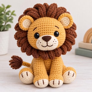 Pode incluir: Um leão de pelúcia feito em crochê com corpo amarelo dourado, uma juba espessa de lã castanho-escura e detalhes em creme nas orelhas, focinho e patas. O leão tem olhos de segurança pretos, nariz bordado em castanho e uma cauda com tufo.