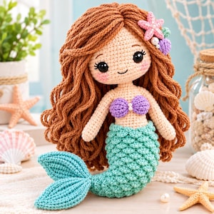 May include: A crocheted mermaid doll with long wavy brown yarn hair, a purple shell-shaped top, and a textured teal green tail. The doll features black safety eyes, pink cheeks, and is decorated with a pink starfish and small purple shells.