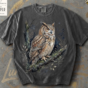 May include: Dark grey Comfort Colors tee with a detailed illustration of an owl perched on a branch. The owl has brown and white feathers, with yellow eyes. The shirt has the text "Comfort Colors Tee" and "Pepper" on a tag.