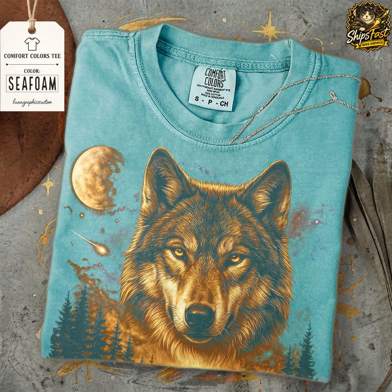 May include: Seafoam Comfort Colors tee featuring a detailed illustration of a wolf with a moon and forest scene. The shirt has the text "Comfort Colors" and "Seafoam" on a tag.