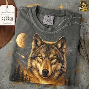 May include: A gray Comfort Colors t-shirt featuring a detailed illustration of a wolf's face with a starry night sky, moon, and trees. The shirt has a Pepper color tag and a small tag with the Comfort Colors logo.