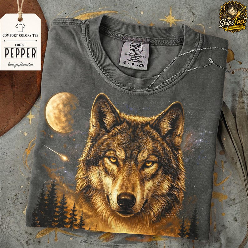 May include: A gray Comfort Colors t-shirt featuring a detailed illustration of a wolf's face with a starry night sky, moon, and trees. The shirt has a Pepper color tag and a small tag with the Comfort Colors logo.